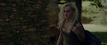 Movie still from “Still” (2018), directed by Takashi Doscher – A woman with dreads is standing in front of a stone wall; Close Up shot, Over the shoulder angle