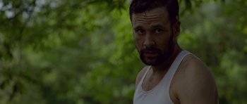 Movie still from “Still” (2018), directed by Takashi Doscher – A person wearing a tank top near a tree; Close Up shot, Over the shoulder angle