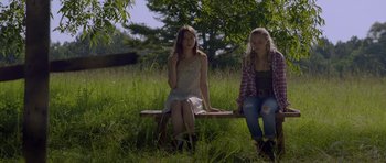 Movie still from “Still” (2018), directed by Takashi Doscher – Two young women sitting on a bench in the grass; Medium shot, Low angle