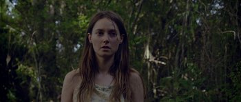 Movie still from “Still” (2018), directed by Takashi Doscher – A woman with long brown hair standing in the woods; Close Up shot, Low angle