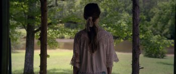 Movie still from “Still” (2018), directed by Takashi Doscher – A woman standing in the grass near a body of water; Medium shot, Over the shoulder angle