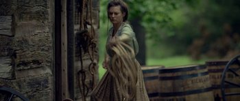 Movie still from “Still” (2018), directed by Takashi Doscher – A woman in a green shirt and brown plaid skirt holding a rope; Medium shot, Over the shoulder angle