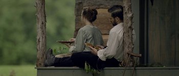 Movie still from “Still” (2018), directed by Takashi Doscher – A man and a woman sitting on a bench eating pizza; Medium shot, High angle