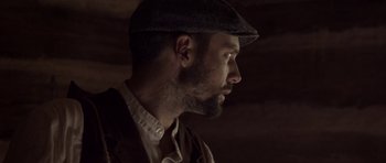 Movie still from “Still” (2018), directed by Takashi Doscher – A man with a beard wearing a hat and jacket; Close Up shot, Low angle