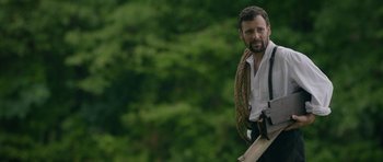 Movie still from “Still” (2018), directed by Takashi Doscher – A man in a white shirt holding a wooden stick; Medium shot, Low angle