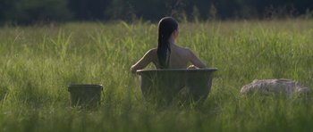 Movie still from “Still” (2018), directed by Takashi Doscher – A woman sitting in a bath tub in the grass; Wide shot, High angle