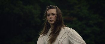 Movie still from “Still” (2018), directed by Takashi Doscher – A woman in a white shirt is standing in a forest; Close Up shot, Low angle