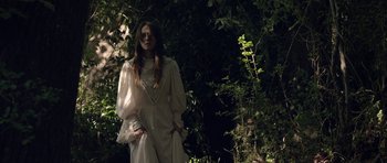 Movie still from “Still” (2018), directed by Takashi Doscher – A woman in a white dress standing next to a tree; Medium shot, Low angle