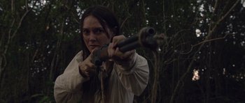 Movie still from “Still” (2018), directed by Takashi Doscher – A woman is holding a gun in the woods; Close Up shot, Over the shoulder angle