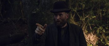 Movie still from “Still” (2018), directed by Takashi Doscher – A man in a hat and a suit points to the side; Medium shot, Over the shoulder angle