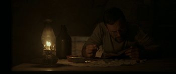 Movie still from “Still” (2018), directed by Takashi Doscher – A man sitting at a table writing on a piece of paper; Medium shot, Low angle