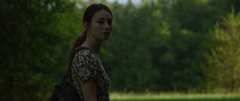 Movie still from “Still” (2018), directed by Takashi Doscher – A woman standing in front of a forest with trees in the background; Close Up shot, Over the shoulder angle