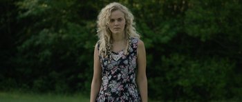 Movie still from “Still” (2018), directed by Takashi Doscher – A woman with blonde curly hair wearing a floral dress; Close Up shot, Over the shoulder angle