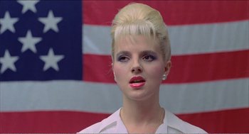 A woman in a white shirt is in front of an american flag