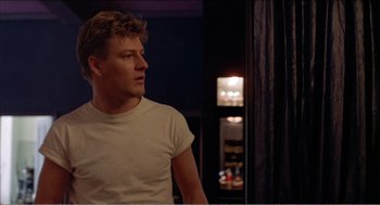 Movie still from “Stormy Monday” (1988), directed by Mike Figgis – A man in a white shirt is looking out a window; Medium shot, Over the shoulder angle