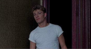 Movie still from “Stormy Monday” (1988), directed by Mike Figgis – A man in a white t - shirt is standing in front of a wall; Close Up shot, Low angle
