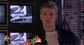 Movie still from “Stormy Monday” (1988), directed by Mike Figgis – A man holding a flower in front of a television; Close Up shot, Over the shoulder angle