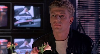 Movie still from “Stormy Monday” (1988), directed by Mike Figgis – A person holding a flower near a television; Close Up shot, Over the shoulder angle