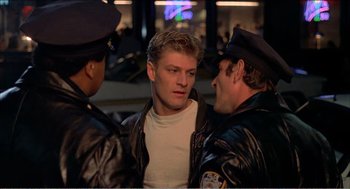 Movie still from “Stormy Monday” (1988), directed by Mike Figgis – Three police officers talking to a man in a leather jacket; Medium shot, Over the shoulder angle