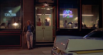 Movie still from “Stormy Monday” (1988), directed by Mike Figgis – A group of people standing in front of a building; Wide shot, Over the shoulder angle
