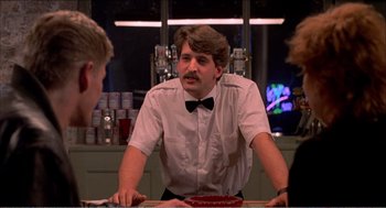 Movie still from “Stormy Monday” (1988), directed by Mike Figgis – A man sitting at a table in front of two other men; Medium shot, Over the shoulder angle
