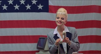 Movie still from “Stormy Monday” (1988), directed by Mike Figgis – A woman holding a phone in front of an american flag; Medium shot, Low angle