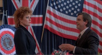 Movie still from “Stormy Monday” (1988), directed by Mike Figgis – A woman and a man are standing in front of an american flag; Medium shot, Low angle