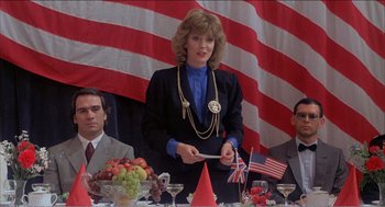 Movie still from “Stormy Monday” (1988), directed by Mike Figgis – A woman standing in front of a group of people at a table; Medium shot, Low angle