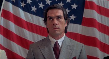 Movie still from “Stormy Monday” (1988), directed by Mike Figgis – A man in a suit and tie in front of a flag; Close Up shot, Low angle
