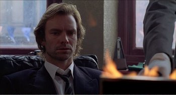 Movie still from “Stormy Monday” (1988), directed by Mike Figgis – A man sitting in front of a fire in a room; Close Up shot, Low angle