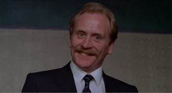 Movie still from “Stormy Monday” (1988), directed by Mike Figgis – An older man with a beard and a mustache wearing a suit and tie; Close Up shot, Low angle