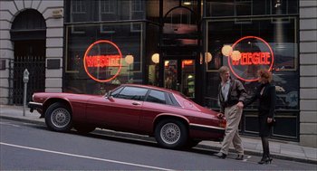 Movie still from “Stormy Monday” (1988), directed by Mike Figgis – A man walking down the street next to a red car; Wide shot, Over the shoulder angle