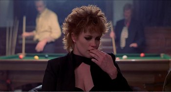 Movie still from “Stormy Monday” (1988), directed by Mike Figgis – A woman in a black jacket is sitting in front of a billiard table; Medium shot, Over the shoulder angle