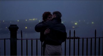 Movie still from “Stormy Monday” (1988), directed by Mike Figgis – A man and a woman kissing on top of a railing; Medium shot, Overhead angle