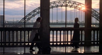 Movie still from “Stormy Monday” (1988), directed by Mike Figgis – Two people walking on a balcony near a bridge; Extreme Wide shot, High angle