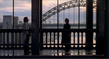 Movie still from “Stormy Monday” (1988), directed by Mike Figgis – Two people are standing on a balcony looking out at a bridge; Extreme Wide shot, High angle