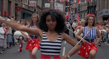 Movie still from “Stormy Monday” (1988), directed by Mike Figgis – A group of people marching down a street with flags; Medium shot, Low angle
