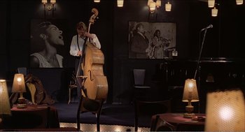Movie still from “Stormy Monday” (1988), directed by Mike Figgis – A man playing a contrabass in front of an audience; Wide shot, High angle