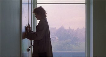 Movie still from “Stormy Monday” (1988), directed by Mike Figgis – A woman standing in front of a window; Medium shot, Over the shoulder angle