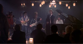 Movie still from “Stormy Monday” (1988), directed by Mike Figgis – A group of people in a room with musical instruments; Wide shot, Over the shoulder angle