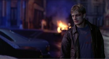 Movie still from “Stormy Monday” (1988), directed by Mike Figgis – A young man standing in front of a fire; Medium shot, Over the shoulder angle
