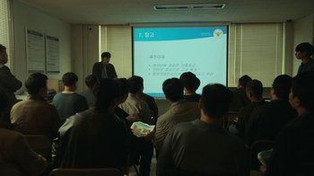 Movie still from “Hellbound” (2021), created by Yeon Sang-ho – A group of people sitting in front of a projector screen; Wide shot, Over the shoulder angle