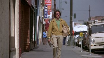 Movie still from “Straight Time” (1978), directed by Ulu Grosbard – A man walking down a street holding a bag of food; Wide shot, Low angle