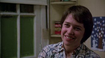 Movie still from “Straight Time” (1978), directed by Ulu Grosbard – A woman smiling for the camera while wearing a plaid shirt; Close Up shot, Over the shoulder angle