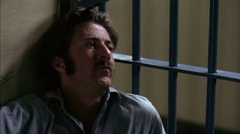 Movie still from “Straight Time” (1978), directed by Ulu Grosbard – A man sitting in front of a metal fence; Close Up shot, Low angle