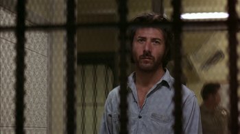 Movie still from “Straight Time” (1978), directed by Ulu Grosbard – A man standing behind bars in front of a window; Close Up shot, Low angle