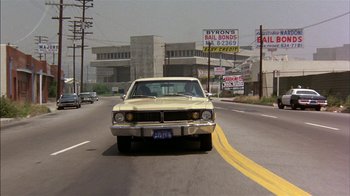 Movie still from “Straight Time” (1978), directed by Ulu Grosbard – An old car driving down the street in the middle of the street; Wide shot, Low angle