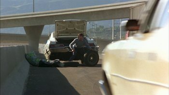 Movie still from “Straight Time” (1978), directed by Ulu Grosbard – A man sitting on the ground next to a white car; Wide shot, Over the shoulder angle