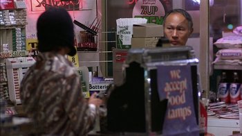 Movie still from “Straight Time” (1978), directed by Ulu Grosbard – Two people are sitting at a counter in a store; Medium shot, Over the shoulder angle