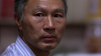 Movie still from “Straight Time” (1978), directed by Ulu Grosbard – An older asian man looking at the camera; Close Up shot, Over the shoulder angle